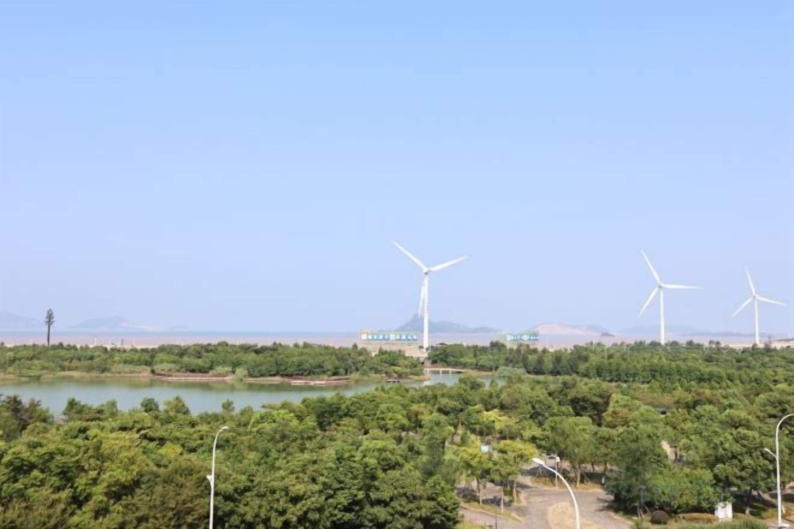 A landscape with wind turbines and a building, surrounded by greenery and a body of water.