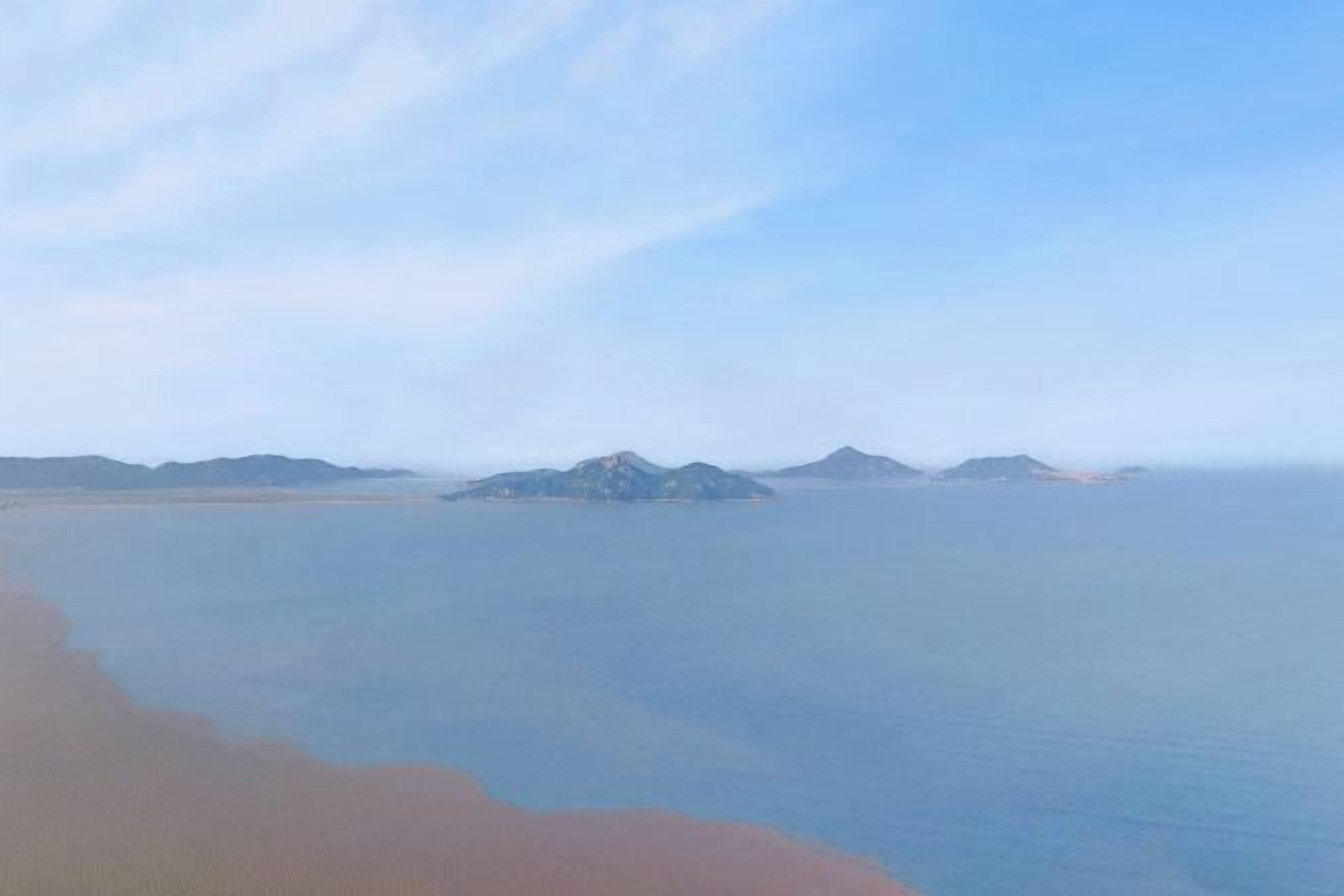 A coastal landscape with a beach and distant mountains.