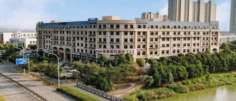 A large, multi-story building with a symmetrical facade, surrounded by greenery and a body of water.