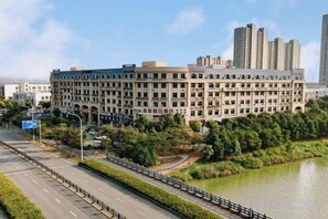 A large, multi-story building with a symmetrical facade, surrounded by greenery and a body of water. - Jie Te holiday inn (Wenling)