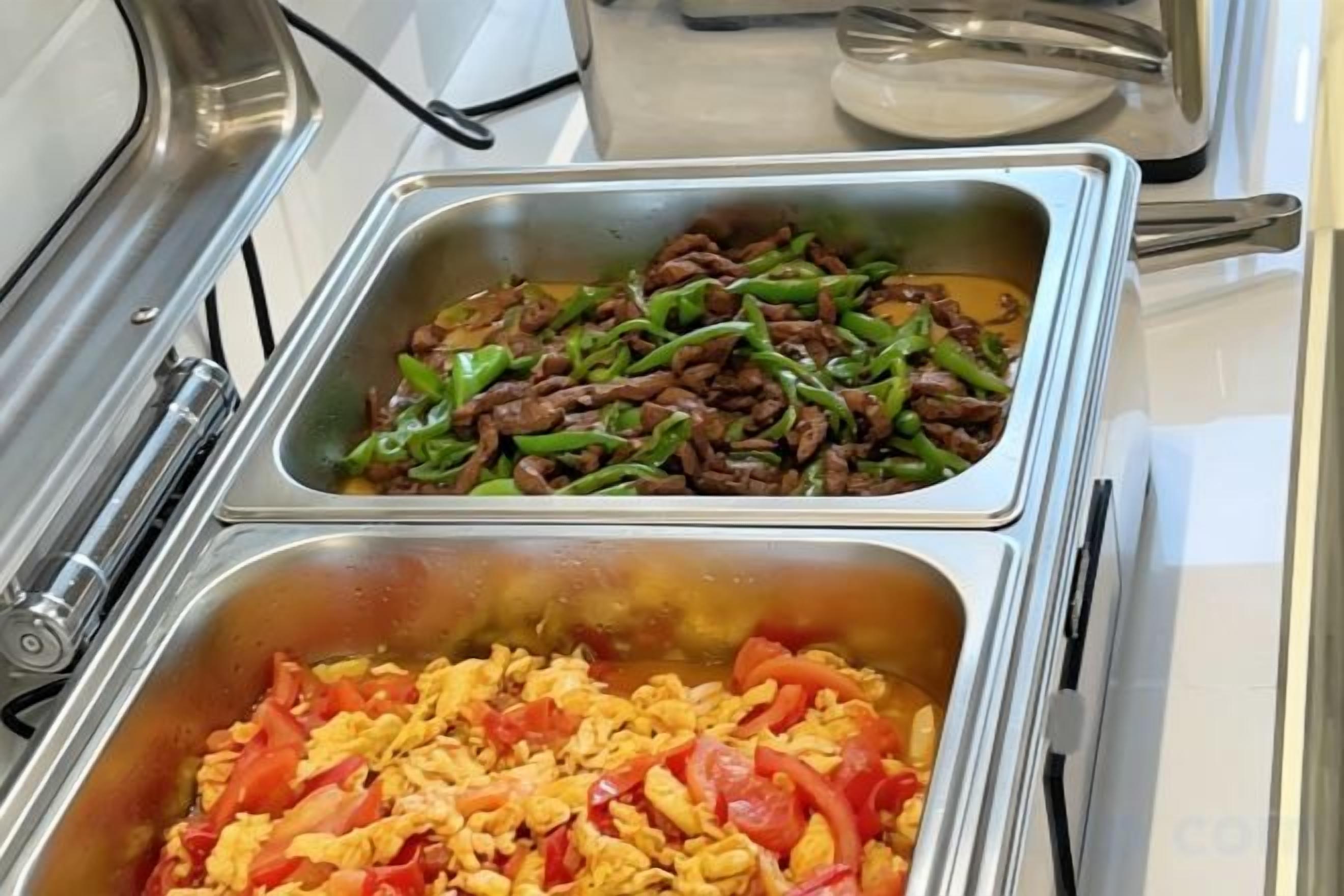 A buffet with two stainless steel serving trays, one with beef and green beans and the other with scrambled eggs and red bell peppers.