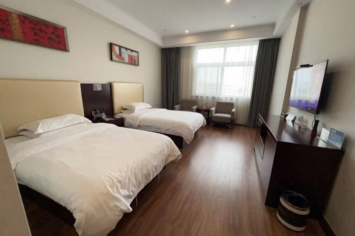 Habitación de hotel con dos camas, un escritorio, una silla, un televisor y una ventana con cortinas.