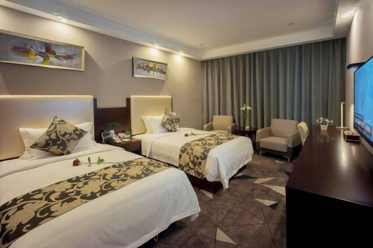 Habitación de hotel con dos camas, un escritorio, una silla, un televisor y obras de arte en las paredes.