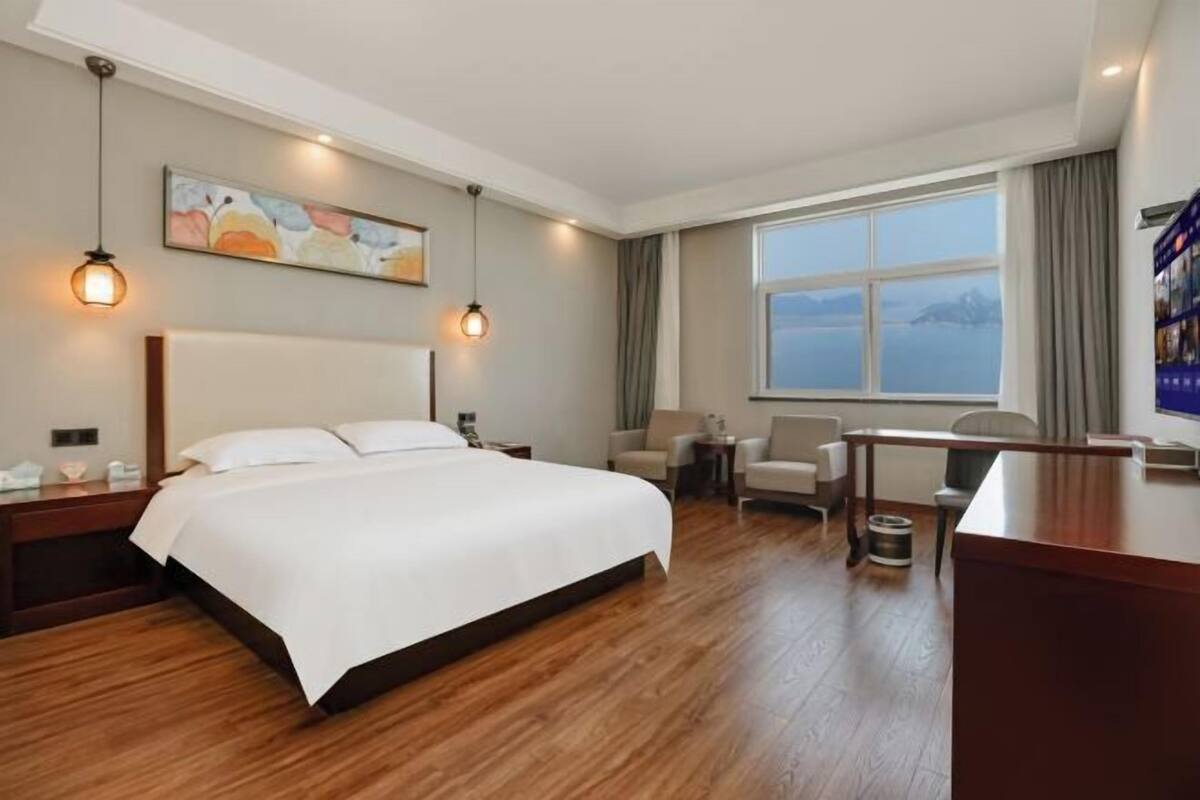Habitación de hotel con una cama grande, un escritorio, una silla, una ventana con vistas y un cuadro en la pared.
