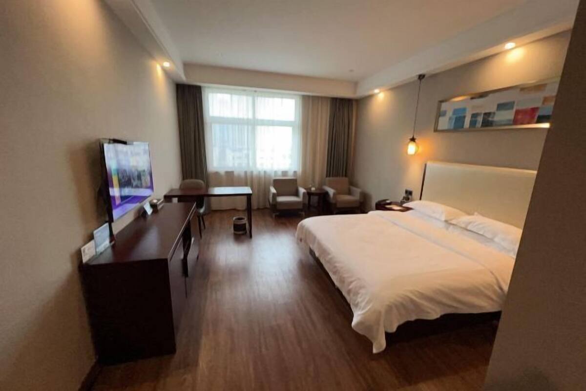 Habitación de hotel con cama, escritorio, silla, televisor y ventana con cortinas.