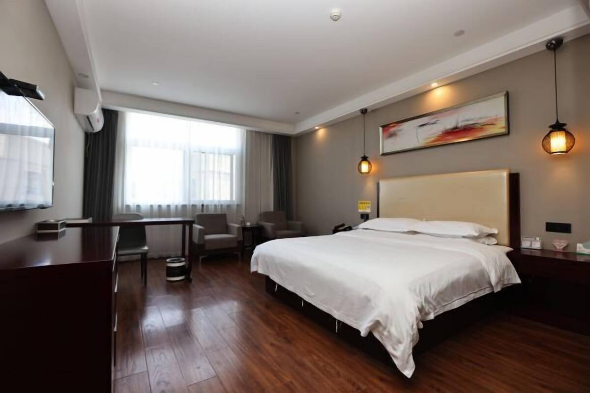 Habitación de hotel con cama, escritorio, sillas y un ventanal grande.