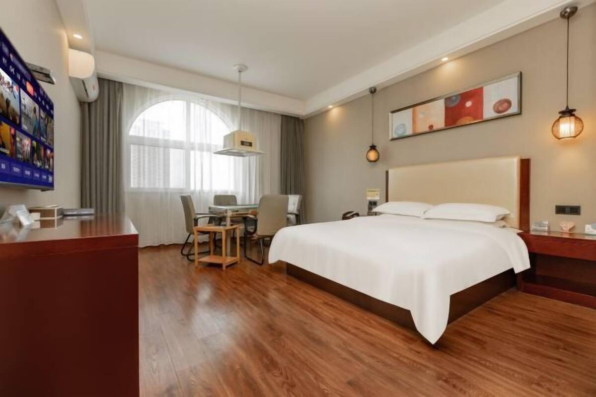 Habitación de hotel con una cama grande, un escritorio con silla, un televisor y una ventana con cortinas.