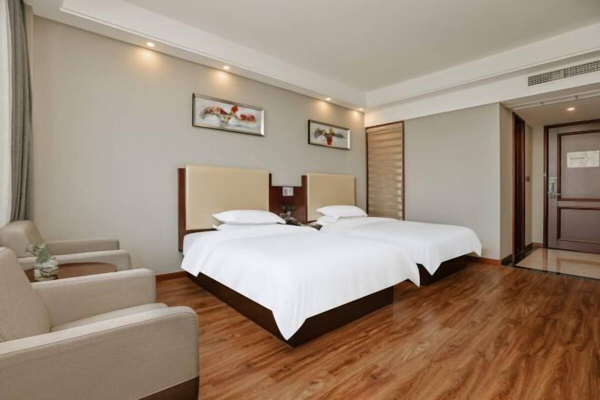 Una habitación de hotel con una cama doble, dos mesitas de noche, una silla y un ventanal grande.