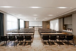 Un salón de conferencias con varias mesas y sillas, una pantalla de proyector y una zona de cocina.