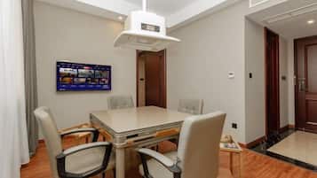 A hotel room with a dining table, four chairs, a television mounted on the wall, and a wooden floor.