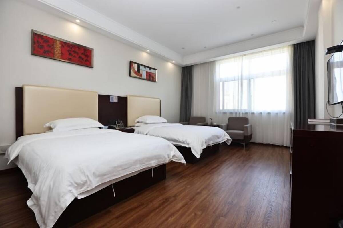 Habitación de hotel con dos camas, un escritorio, una silla y un amplio ventanal con cortinas.