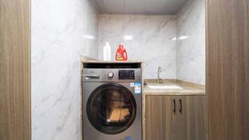 A compact laundry room with a washing machine, a sink, and wooden cabinets.