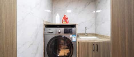 A compact laundry room with a washing machine, a sink, and wooden cabinets.