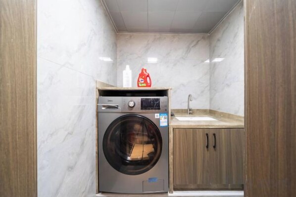 A compact laundry room with a washing machine, a sink, and wooden cabinets. - Xiamen Kangheng Yijing Hotel (Gaoqi Airport Houpu Subway Station) (Xiamen)