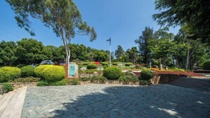 A paved pathway leading to a building with a stone facade, surrounded by well-maintained greenery and trees.