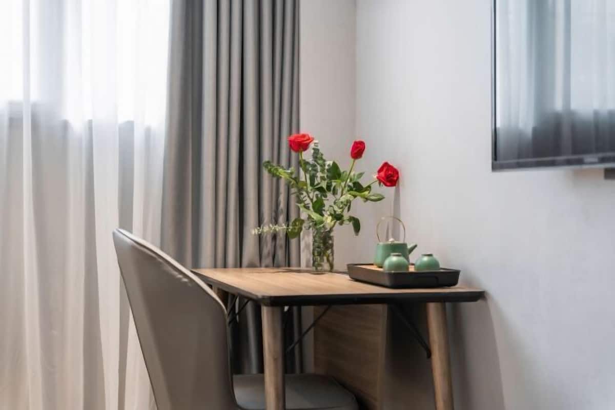A room with a table, a chair, a vase with flowers, and a wall-mounted television.