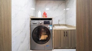 A compact laundry room with a built-in washing machine, a sink, and wooden cabinets.