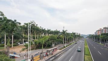 A wide road with a sidewalk on one side, lined with trees and buildings.
