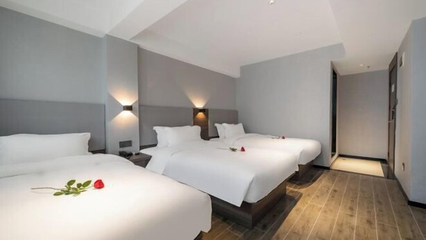 A hotel room with three beds, a wooden floor, and a modern design.