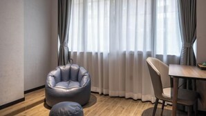 A room with a large window, a leather bean bag chair, a dining table with chairs, and a small round ottoman.