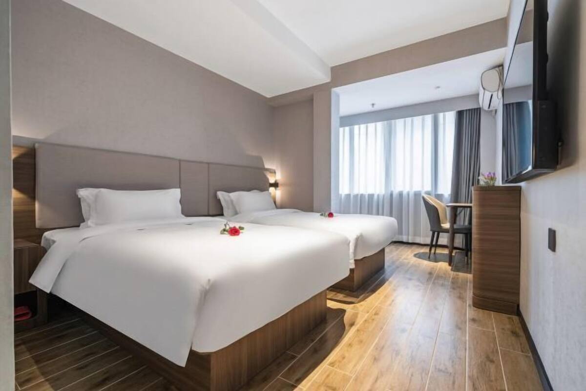 A hotel room with two beds, a desk, a chair, a television, and a large window with curtains.