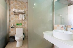 Ein Badezimmer mit Toilette, Waschbecken und Spiegel. Über der Toilette befindet sich ein Handtuchhalter und daneben ein Mülleimer.