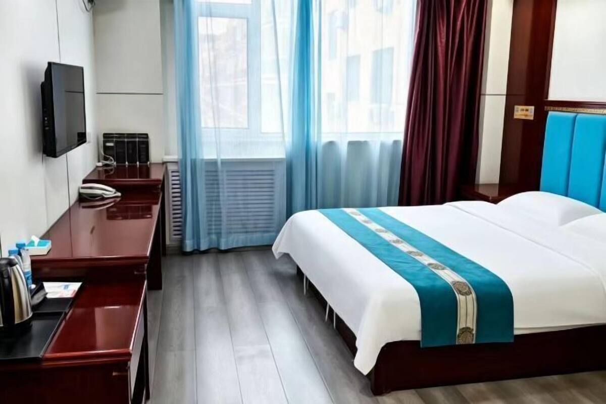 Een hotelkamer met een bed, een bureau, een televisie en een raam met gordijnen.