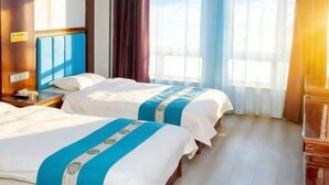 Une chambre d’hôtel avec deux lits, une tête de lit en bois, une table de chevet et une grande fenêtre avec des rideaux.