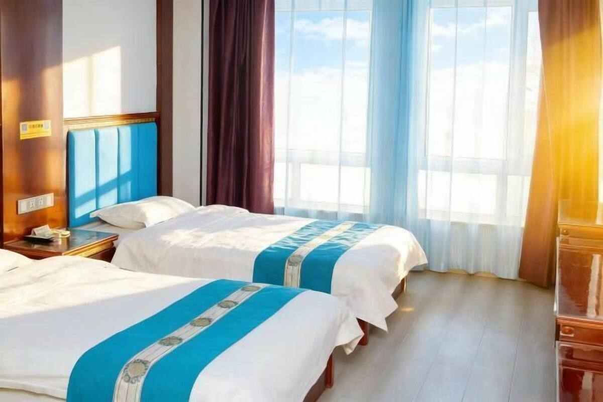 Een hotelkamer met twee bedden, een houten hoofdbord, een nachtkastje en een groot raam met gordijnen.