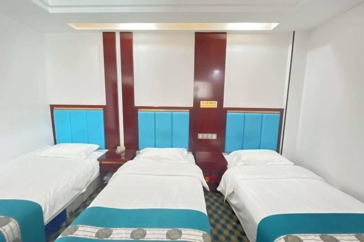 Een hotelkamer met drie eenpersoonsbedden, elk met een blauwe hoofdbord en witte beddengoed. Er zijn houten panelen op de muren en een kleine tafel tussen de bedden.