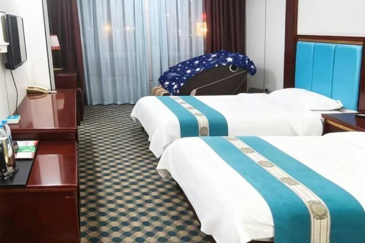 Een hotelkamer met twee bedden, een bureau, een stoel, een televisie en een raam met gordijnen.