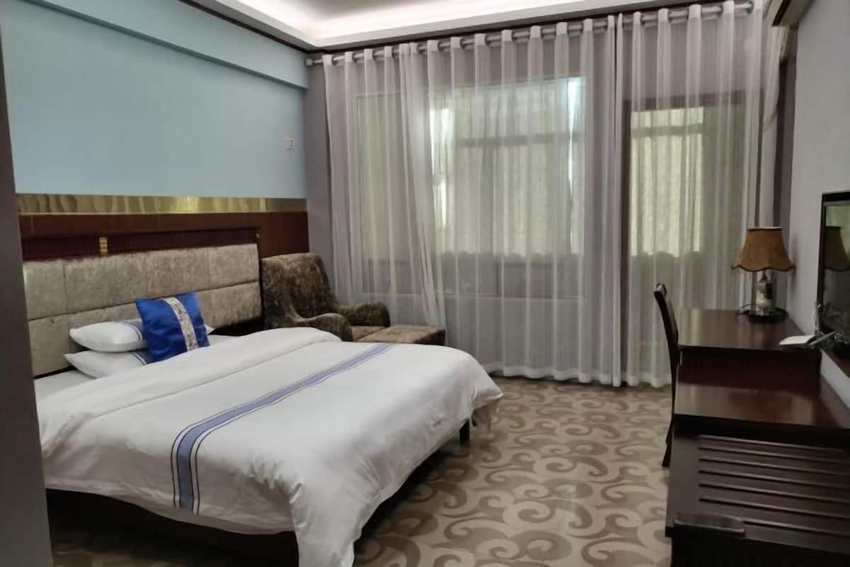 Habitació d'hotel amb llit, escriptori, cadira i finestra amb cortines.