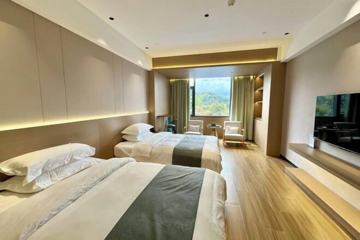 Habitació d'hotel amb tres llits, televisió, escriptori i finestra amb cortines.