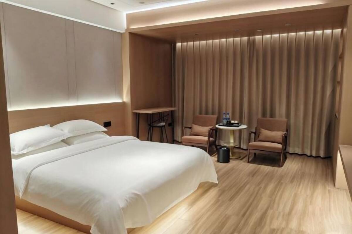 Habitació d'hotel amb un llit, dues butaques, una taula petita i una cortina.