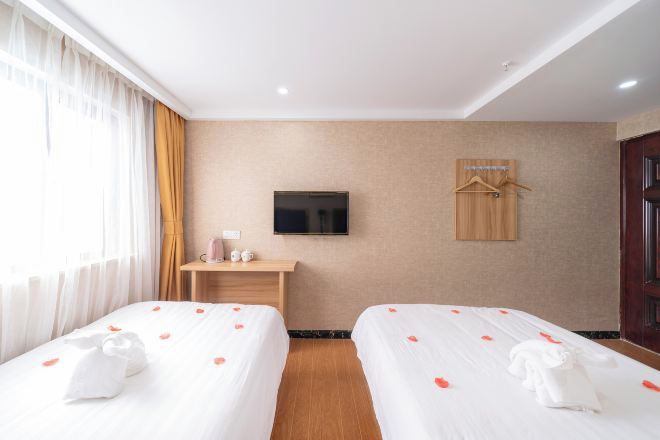 A hotel room with two beds, a TV, a wooden desk, and a coat rack.