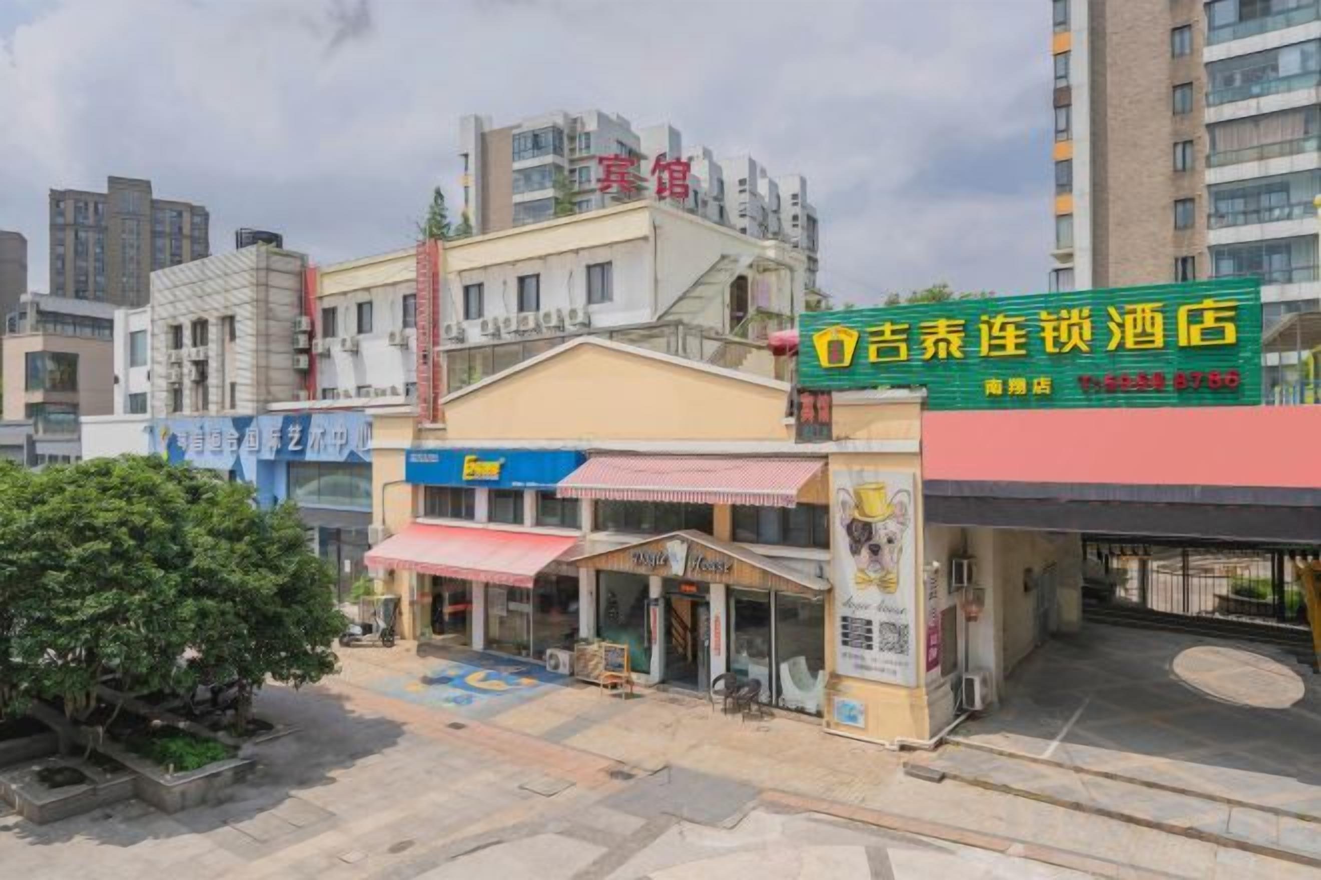 A hotel with a red and yellow facade, a visible entrance, and a small outdoor seating area.