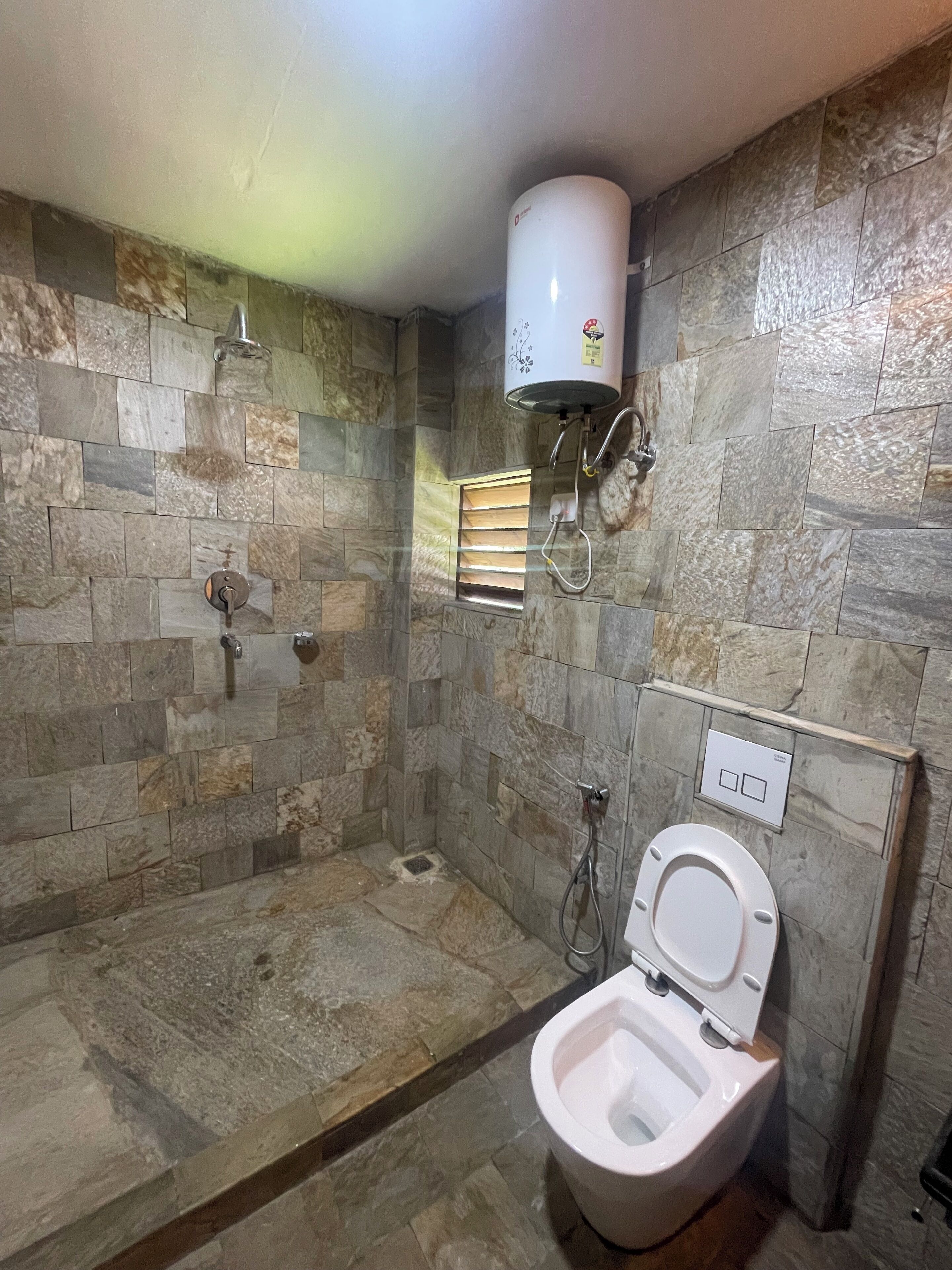 Une salle de bain avec un mur en pierre, une douche, des toilettes et un chauffe-eau.