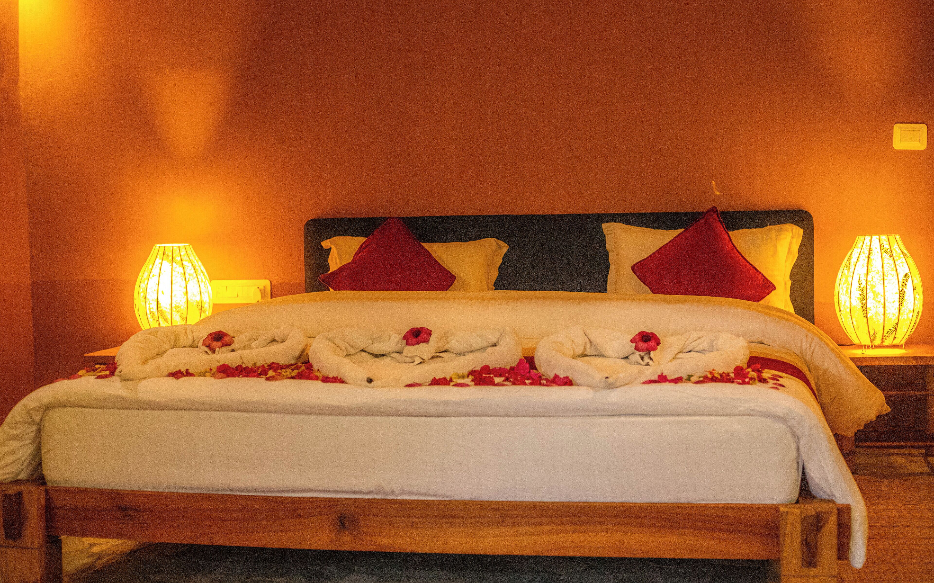 A neatly made bed with white linens and red pillows, a wooden headboard, and two bedside lamps.