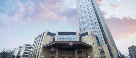 A modern building with a prominent entrance and a tall skyscraper in the background.