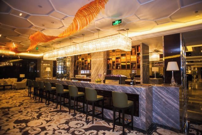 Un espace bar doté d’un comptoir en marbre, de plusieurs tabourets et d’un tapis à motifs.