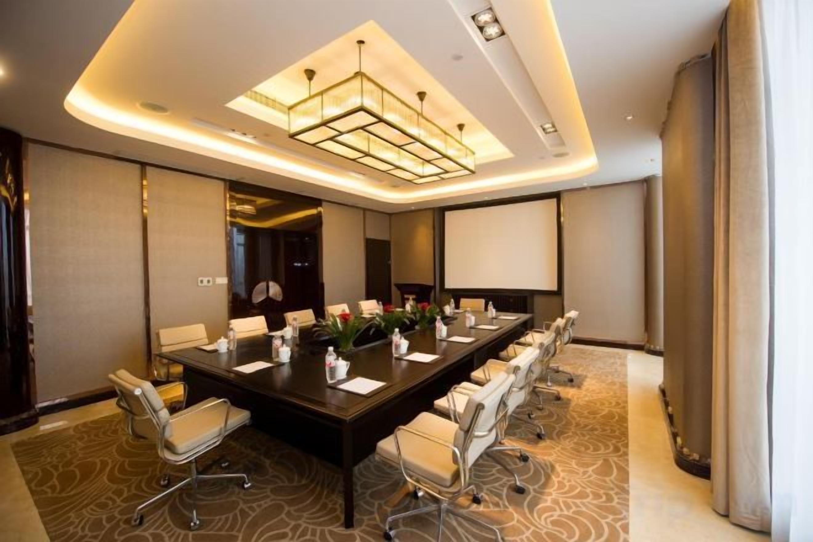 A conference room with a long table, chairs, a projector screen, and a modern chandelier.