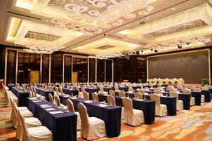 A conference room with rows of tables and chairs, a large screen, and a decorative ceiling.