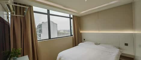 A hotel room with a bed, a desk, and a window with curtains.