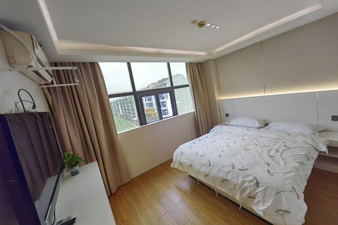 Un dormitorio con un ventanal grande, una cama con ropa de cama blanca, una mesita de noche y un aire acondicionado de pared.
