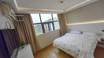 Un dormitorio con un ventanal grande, una cama con ropa de cama blanca, una mesita de noche y un aire acondicionado de pared.