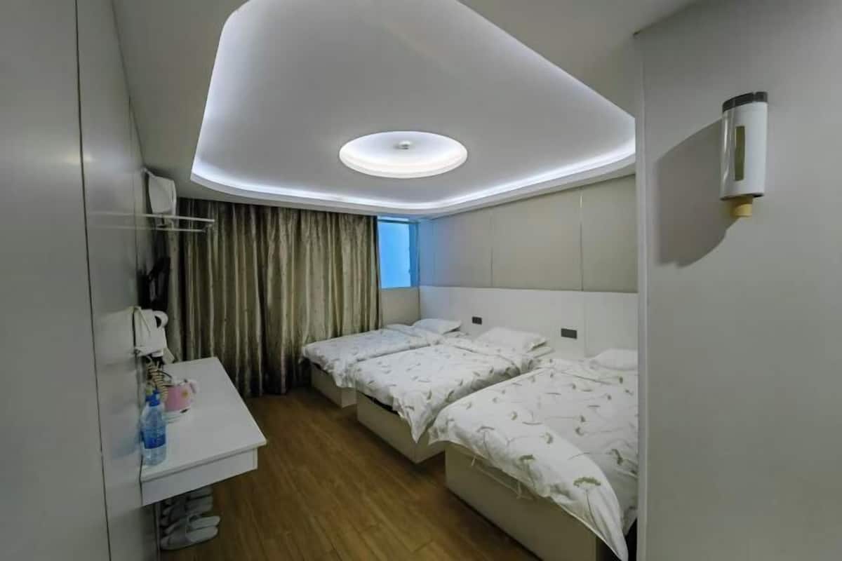 A hotel room with a modern design, featuring a white bed, a bedside table with a water bottle, a mirror, and a window with curtains.