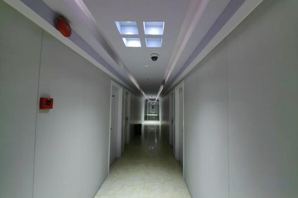 A narrow, well-lit hallway with a ceiling light fixture and a fire alarm on the left wall. - Langang Zhixing Hostel (Shanghai)