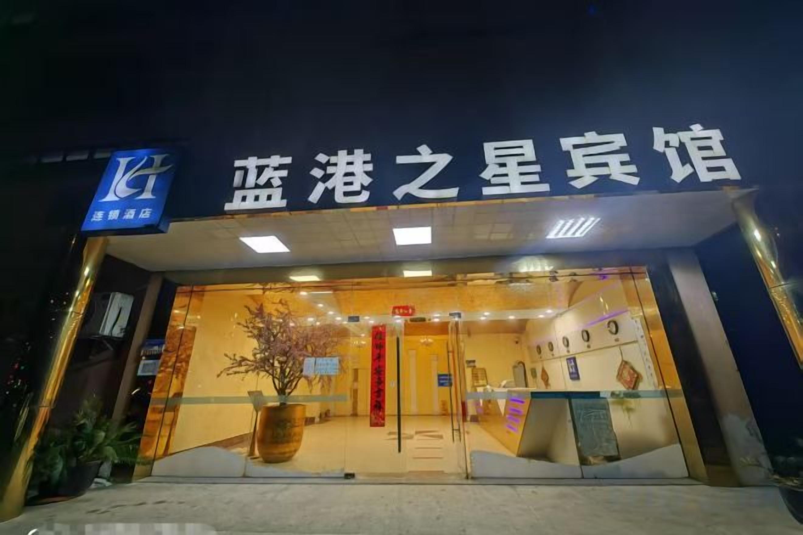 A hotel entrance with a sign in Chinese characters, a reception desk, and a potted plant.