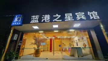 A hotel entrance with a sign in Chinese characters, a reception desk, and a potted plant.