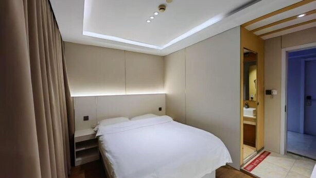 Quarto de hotel com uma cama, mesa de cabeceira, guarda-roupa e banheiro visível através de uma porta aberta.